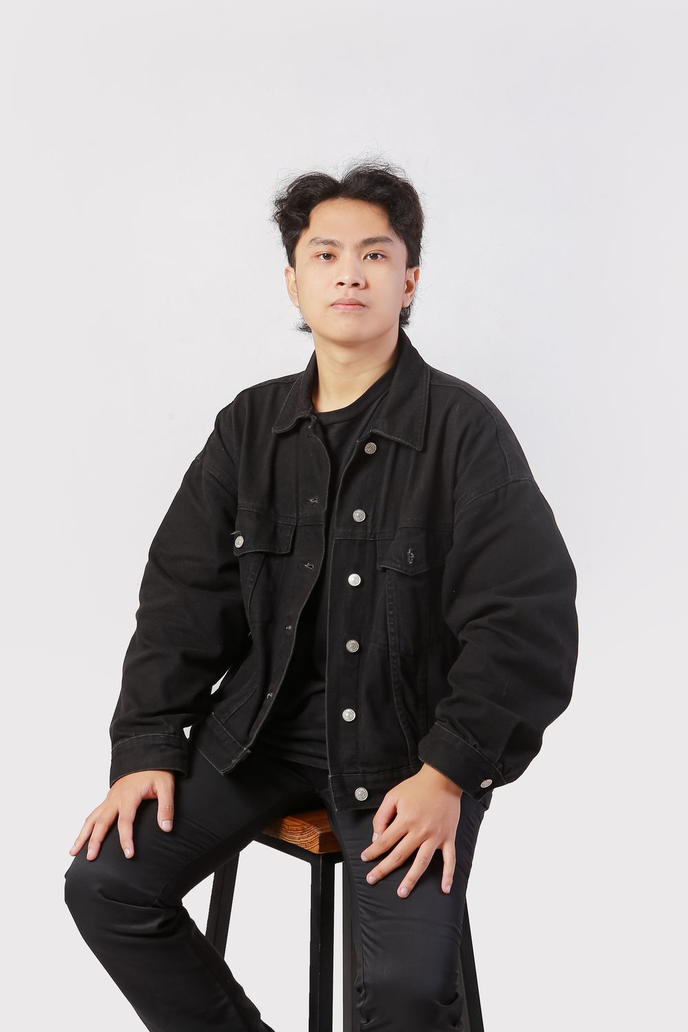 Rizky Ahmad Ramadan seated on a stool, in a black denim jacket